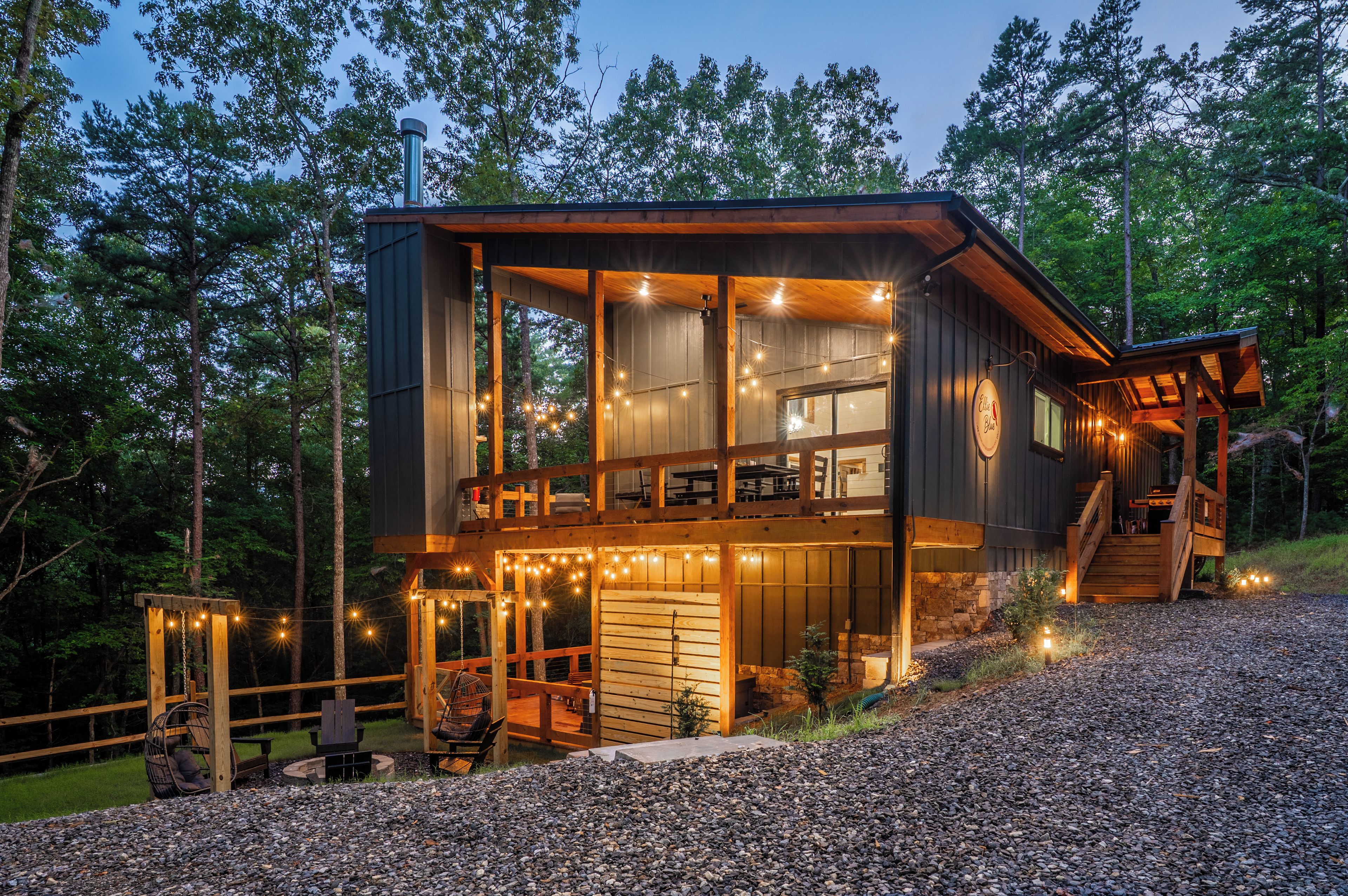 A cabin with a deck, outdoor seating, and a stone foundation.