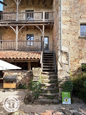 A stone building with a wooden balcony, a staircase, and a sign indicating it's a Gîte. - Les Teulières Vacation Rental - SAINT CIRGUES (SAINT CIRGUES)