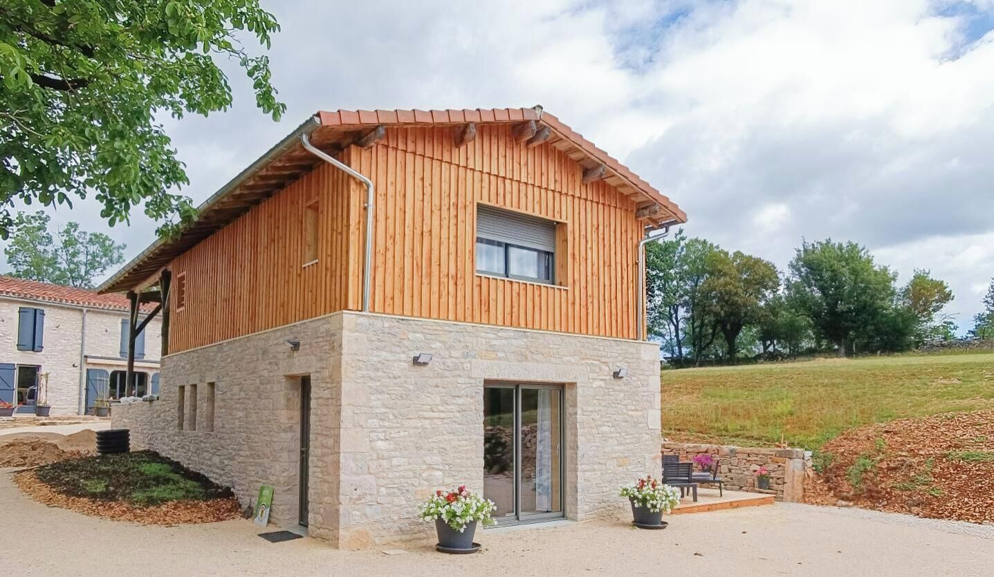 A modern two-story building with a stone base and wooden upper structure, featuring a large window and a door.