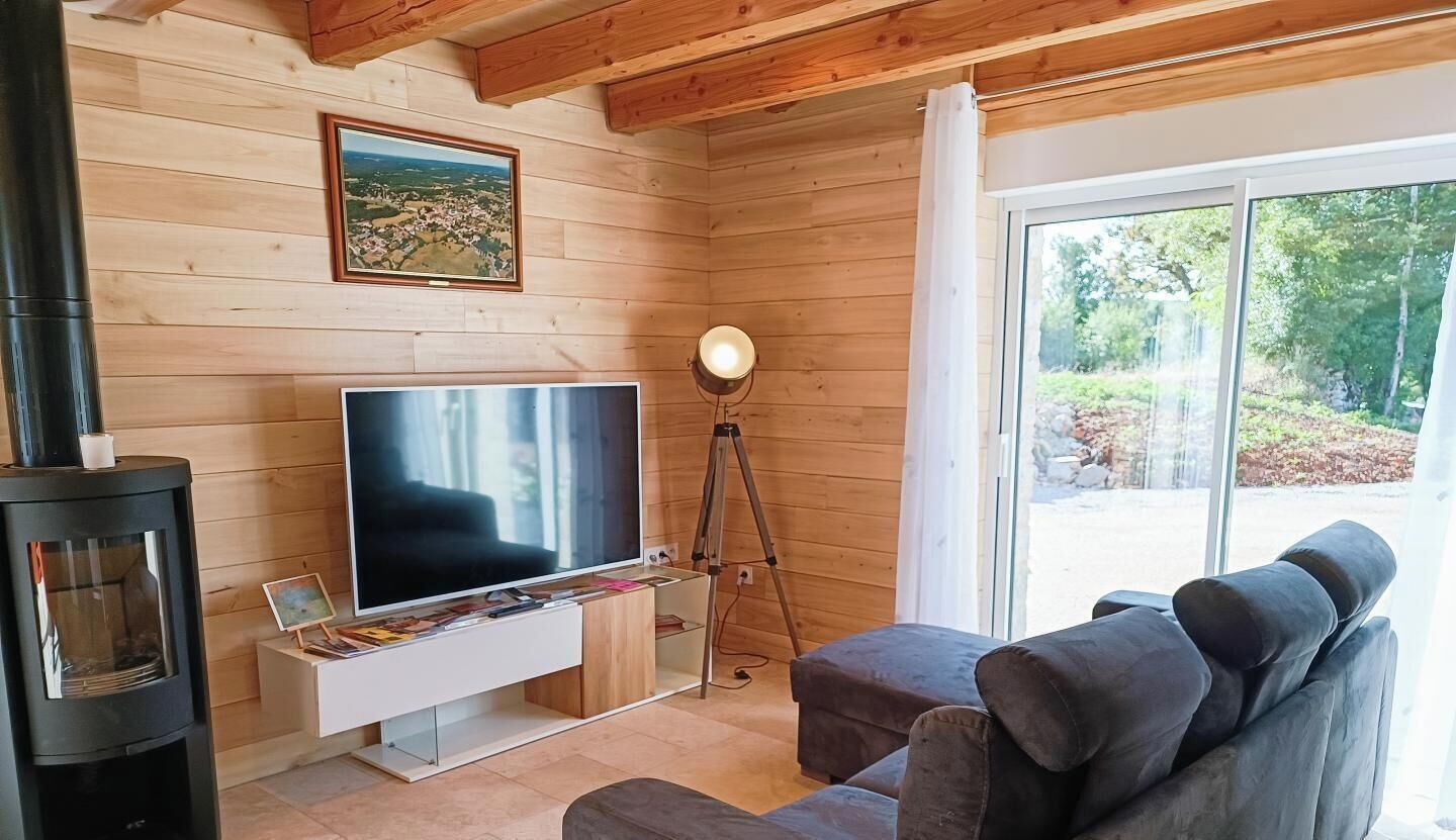 A modern living room with a large flat-screen TV, a wooden wall, a fireplace, and a large window.