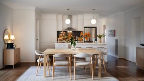 A modern kitchen with white cabinetry, a wooden dining table with six chairs, and a vase with flowers on the table.