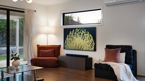 Ein modernes Wohnzimmer mit Glastisch, einer Couch, einem Sessel, einer Stehlampe, einem Flachbildfernseher und einem großen abstrakten Gemälde.