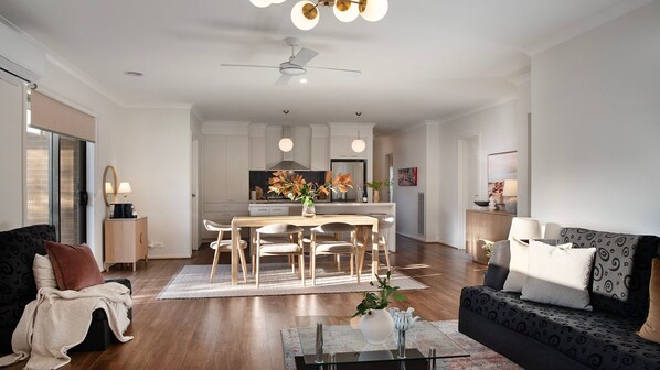 A modern living room with a dining area, a sofa, a coffee table, and a ceiling fan.