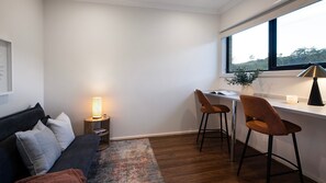 Ein modernes Zimmer mit einer Couch, zwei Sesseln, einem Schreibtisch, einer Lampe und einem Fenster mit Blick.