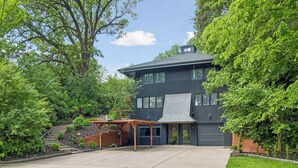 A modern two-story house with a large garage, surrounded by lush greenery.