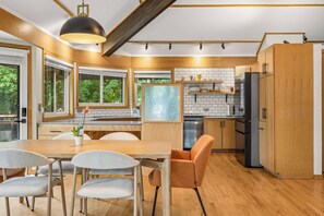 A modern kitchen with wooden cabinets, a dining table with chairs, and a large window.