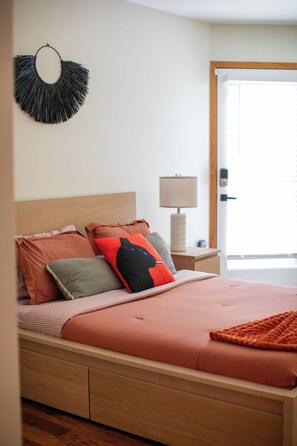 A bedroom with a bed, pillows, a bedside table, a lamp, and a door.