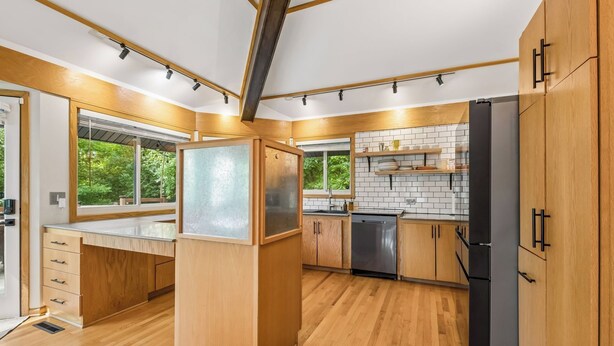 A modern kitchen with wooden cabinets, a black refrigerator, and a window with a view of greenery.