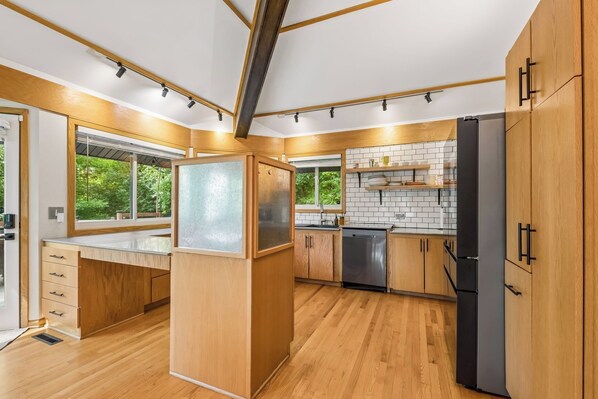 A modern kitchen with wooden cabinets, a black refrigerator, and a window with a view of greenery.