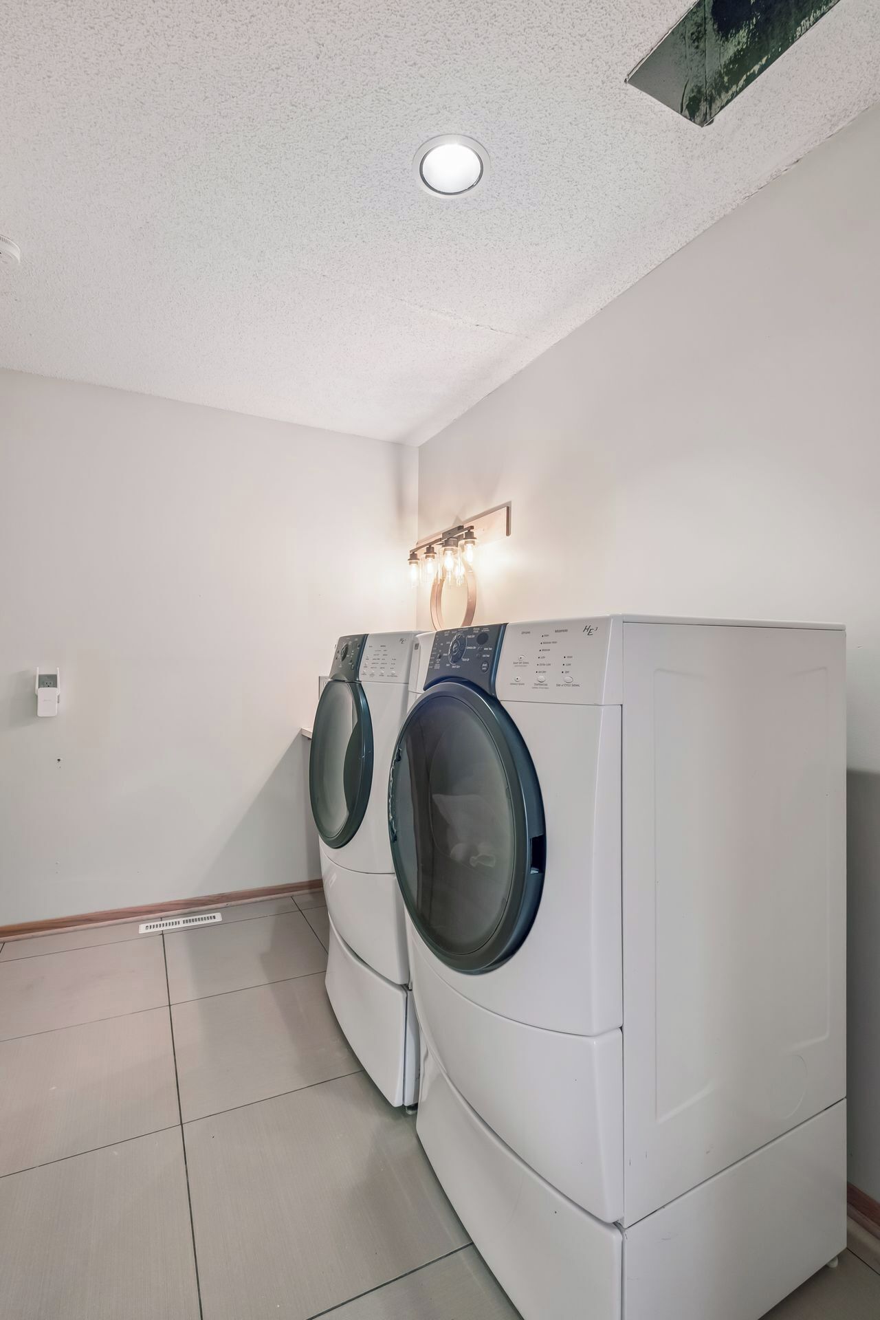 Une buanderie équipée de deux machines à laver à chargement frontal, d’un luminaire et d’une prise de courant murale.