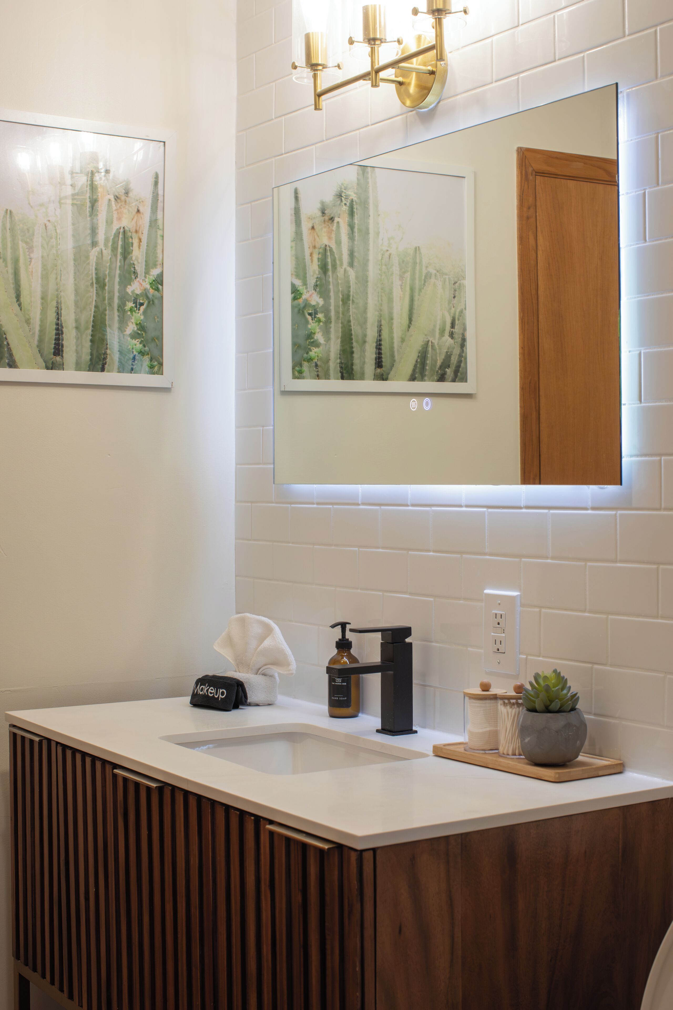Une salle de bain moderne avec un meuble-lavabo blanc, un miroir, une serviette, un distributeur de savon et une petite plante en pot.