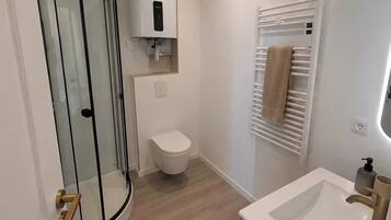 Une salle de bain avec une douche à parois de verre, des toilettes, un lavabo avec un miroir et un porte-serviettes.