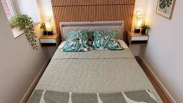 Une chambre à coucher comprenant un lit, une tête de lit, des tables de chevet, des lampes et une plante fixée au mur.