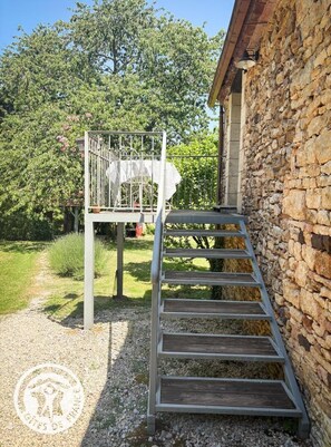 Eine Treppe führt zu einem Balkon mit Metallgeländer, einer Steinmauer und einem Gartenweg.