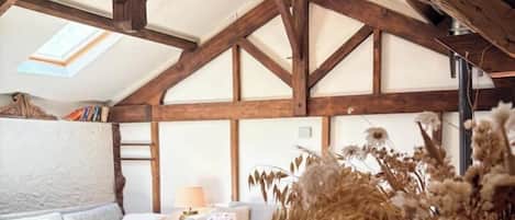 A loft-style room with exposed wooden beams, a skylight, a sofa, a table, and a vase with dried flowers.