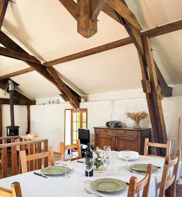 Ein Essbereich mit Tisch für vier Personen, Holzbalkendecke, Kamin und rustikalem Dekor.