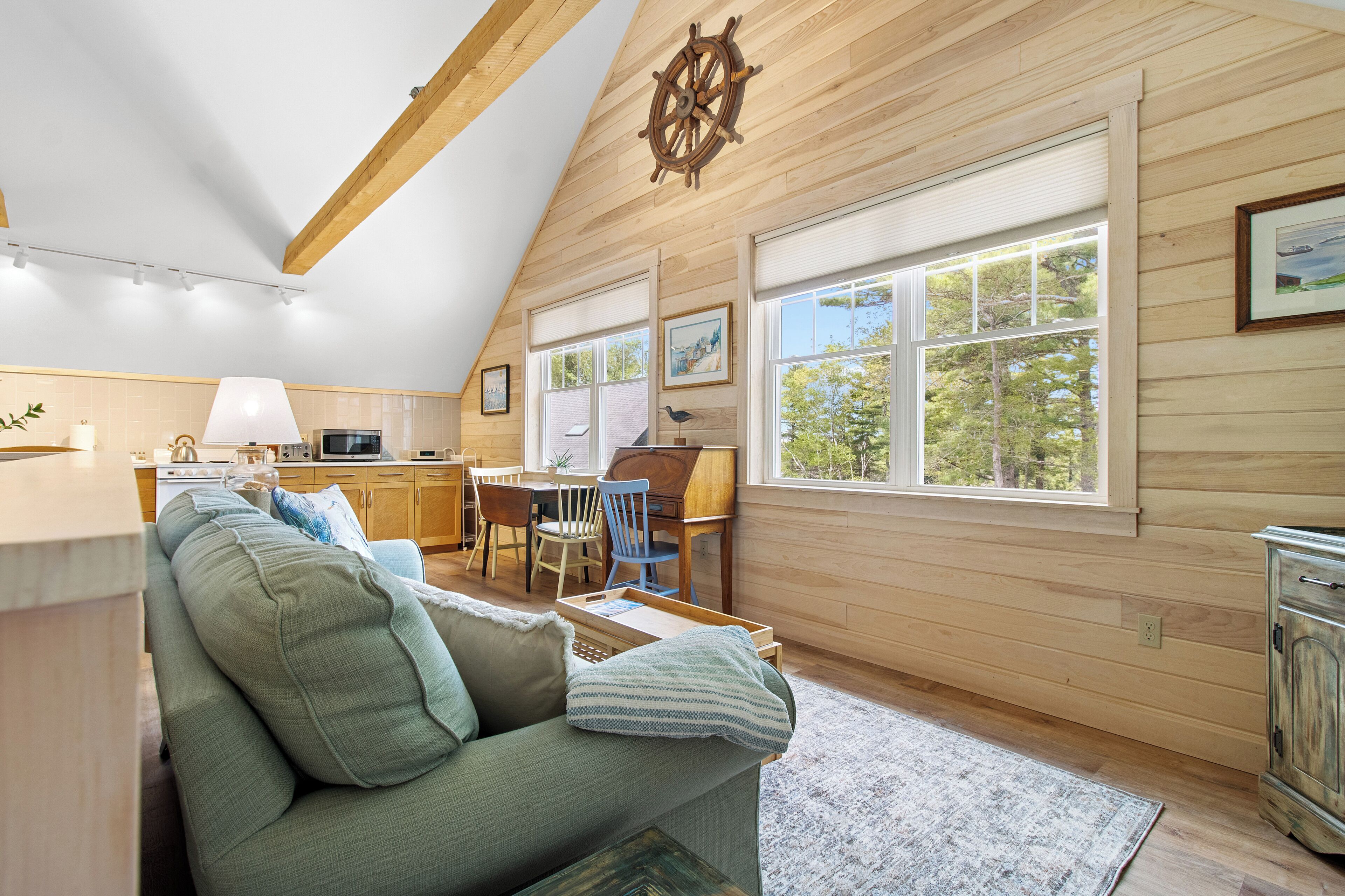 L’intérieur chaleureux d’un chalet avec un plafond en bois, un coin repas, un canapé et une vue sur l’extérieur.