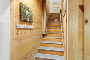 A wooden staircase with a metal handrail, a wall-mounted coat rack, and a framed picture. - Bent River Guest Quarters - River-view couple retreat with kitchen, patio, AC, Wi-Fi (Cushing)