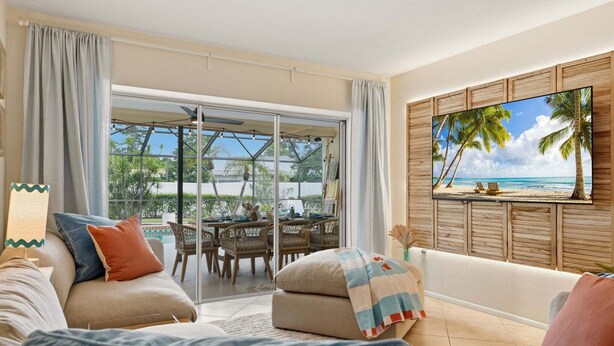 Ein Wohnzimmer mit einer Couch, einem Fernseher und Blick auf einen Strand durch eine Glastür.