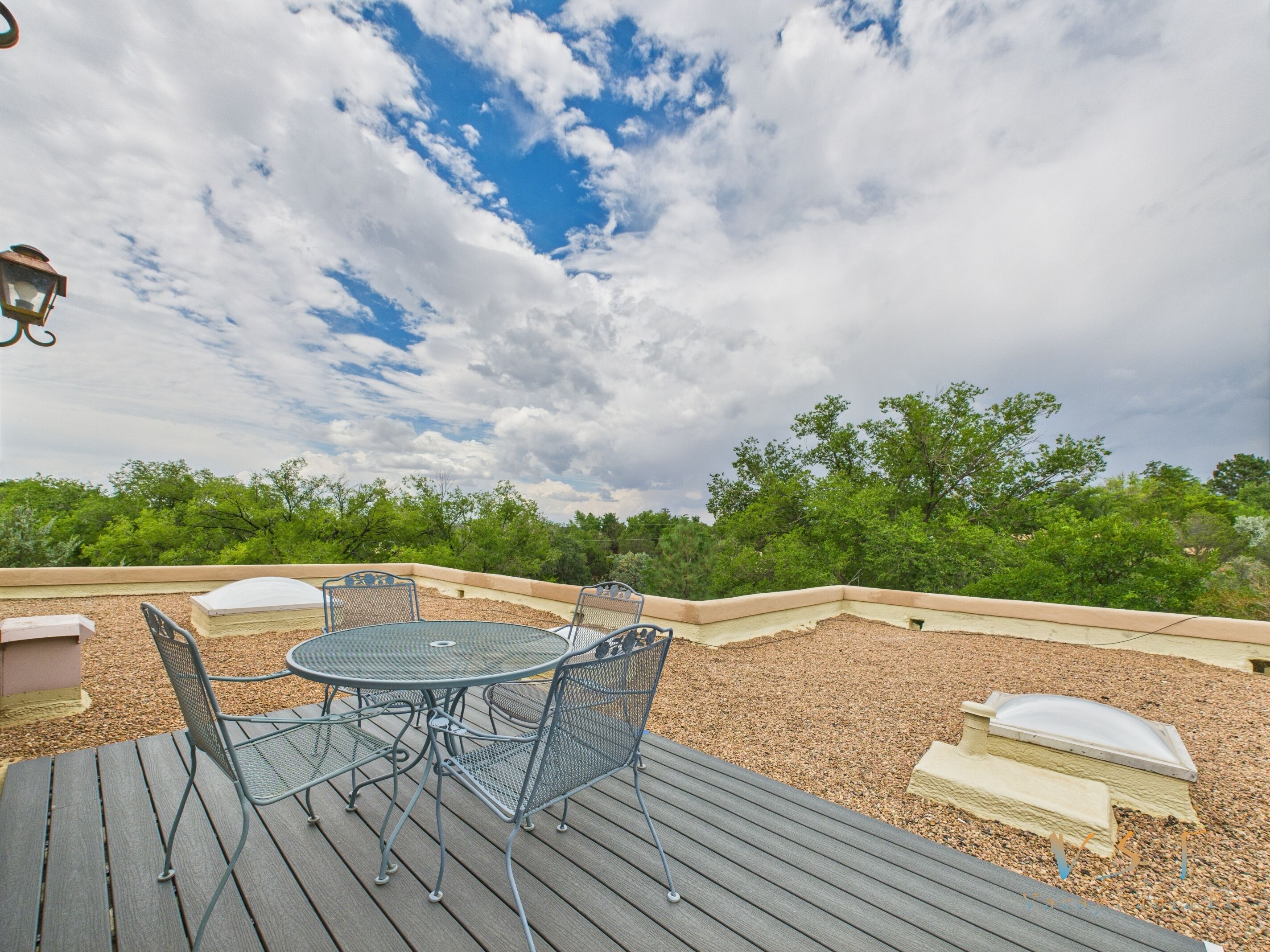 An outdoor patio with a round table and chairs, surrounded by a wooden deck and a low wall.