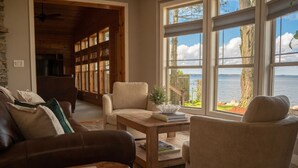 Un salon chaleureux avec vue sur l’eau, une cheminée et une bibliothèque.
