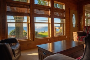 A room with large windows, a wooden table, a leather chair, and a patterned sofa.