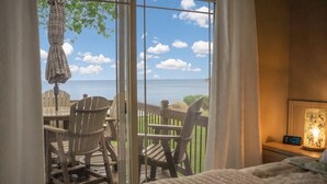 Une chambre avec vue sur la mer, grâce à de grandes fenêtres, une terrasse en bois avec des chaises et une table.