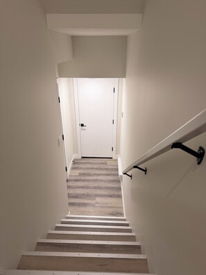Una escalera con escalones de madera y paredes blancas que conduce a una puerta cerrada en la parte superior.