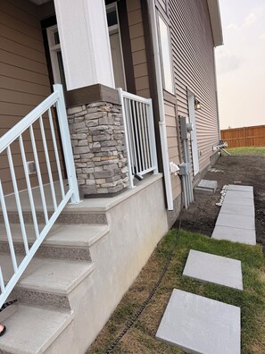 A residential house with a stone accent wall, a white railing on the front steps, and a concrete pathway leading to the entrance. - Cozy 2-Bedroom apartment offering comfort, convenience & exceptional value (Calgary)
