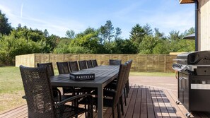 Eine Terrasse im Freien mit Holzdeck, Tisch mit Stühlen und Grill.