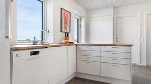 A modern kitchen with white cabinetry, a dishwasher, a sink with a faucet, and a window providing natural light. - VillaVilla 981 - Hostrup Strand, Limfjorden (Spøttrup)