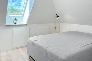 Ein Schlafzimmer mit Dachfenster, einem Bett, einer Stehlampe und einer Heizung.