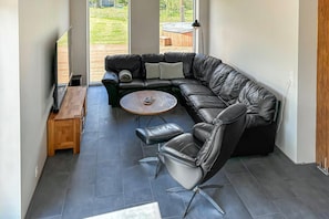 Ein modernes Wohnzimmer mit einer Ledersofa, einem Holztisch und einem Fernseher auf einem Standfuß.