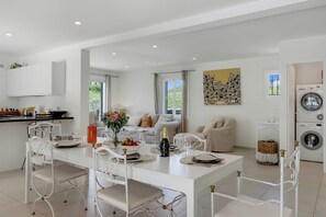 A modern kitchen with white cabinetry, a dining area with a white table set for six, and a living area with a sofa and a painting. - Villa Roi Soleil Private pool - St-Tropez, Saint-Tropez, France (Saint-Tropez)