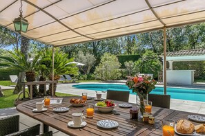 An outdoor dining area with a pool view, wooden tables, chairs, and a covered patio. - Villa Roi Soleil Private pool - St-Tropez, Saint-Tropez, France (Saint-Tropez)