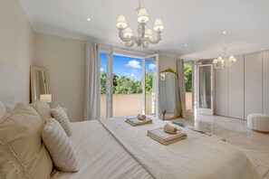 Ein geräumiges Schlafzimmer mit einem großen Bett, einer Chandelier und Blick durch die offene Tür.