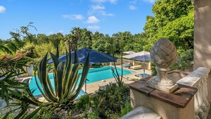 Une piscine entourée de verdure, une balustrade en pierre et un vase décoratif.