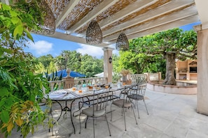 Ein Essbereich im Freien mit einem Tisch für vier Personen, umgeben von Stühlen, unter einer Pergola mit hängenden Laternen.