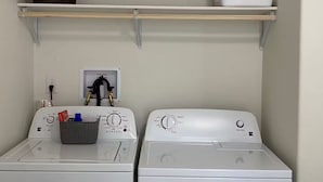 A laundry area with two white front-loading washers, a shelf with a basket, and a white laundry basket.