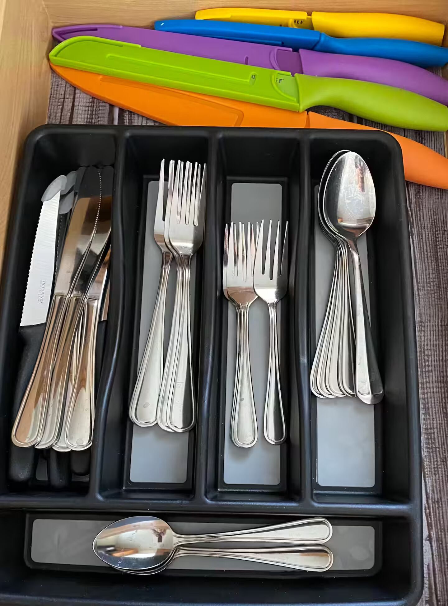 Una bandeja negra con compartimentos que contiene cubiertos, incluyendo tenedores, cuchillos y cucharas.