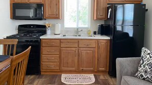 A kitchen with wooden cabinets, a black stove, a microwave, a refrigerator, a sink, and a window with blinds.