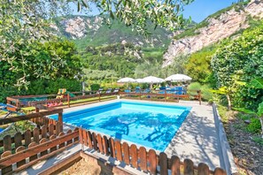 A swimming pool with a wooden deck and lounge chairs, surrounded by greenery and mountains. - Lagotissimo 17 - Apartment with Balcony View and Pool, Riva del Garda, Italy (Riva del Garda)