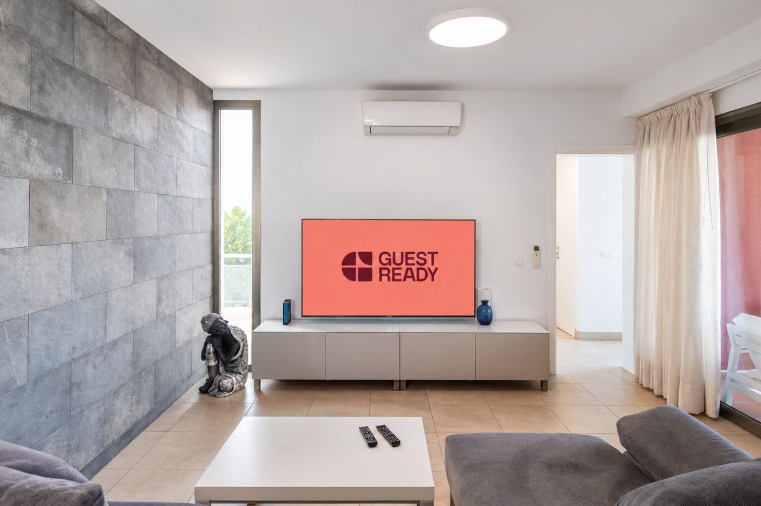 A modern living room with a flat-screen TV displaying 'GUEST READY,' a white console table, a statue, and a sofa.