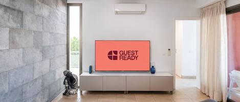 A modern living room with a flat-screen TV displaying 'GUEST READY,' a white console table, a statue, and a sofa.