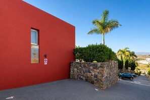 A red building with a stone wall, a palm tree, and a parking area. - GuestReady - Villa Salobre Par4 Private Pool (San Bartolomé de Tirajana)