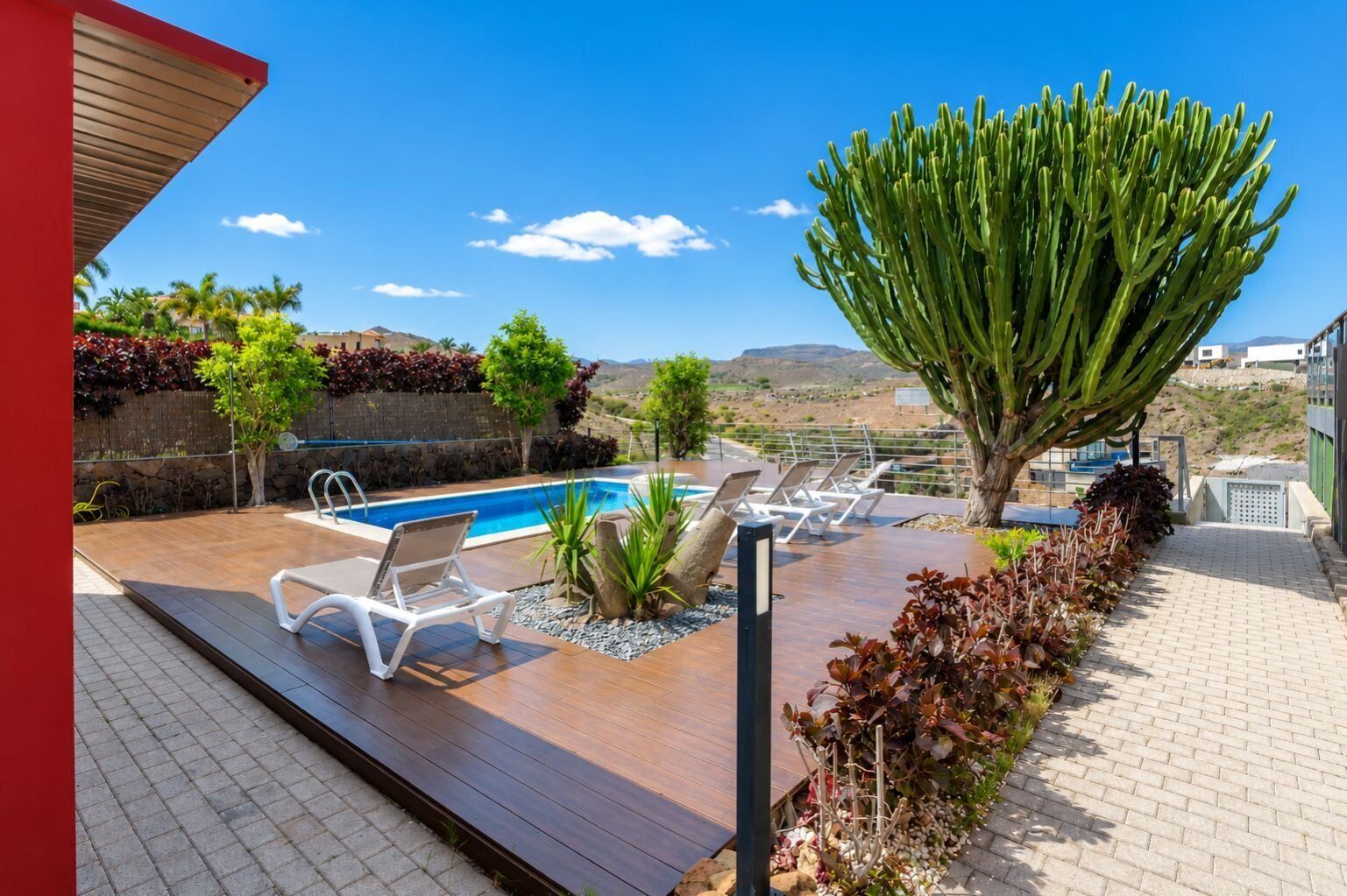 Zona de piscina con sillones de descanso, un cactus y vistas del paisaje.