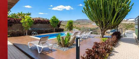 Zona de piscina con sillones de descanso, un cactus y vistas del paisaje.