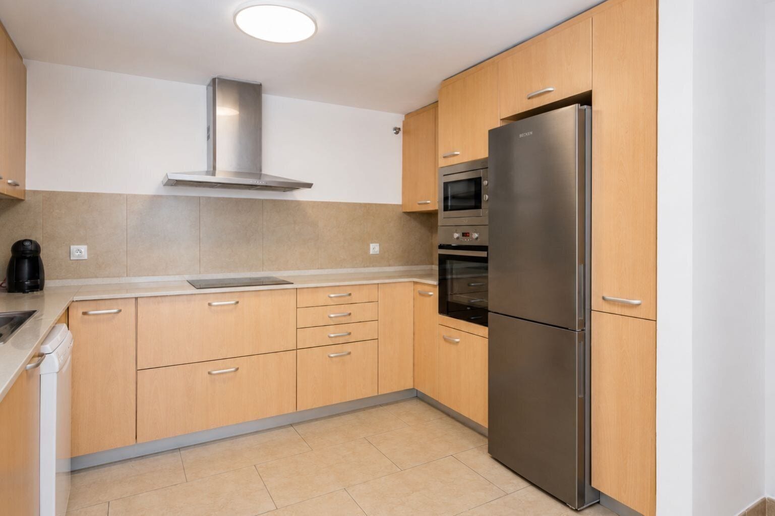 Eine moderne Küche mit Holzschränken, einem Edelstahlkühlschrank, einem Backofen und einer eingebauten Mikrowelle.