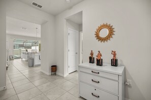 Un intérieur moderne avec une commode blanche, un miroir en forme de soleil et un couloir menant à un espace cuisine.