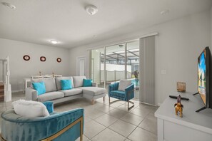 Un salon moderne avec un canapé d’angle, un fauteuil bleu et un téléviseur à écran plat.